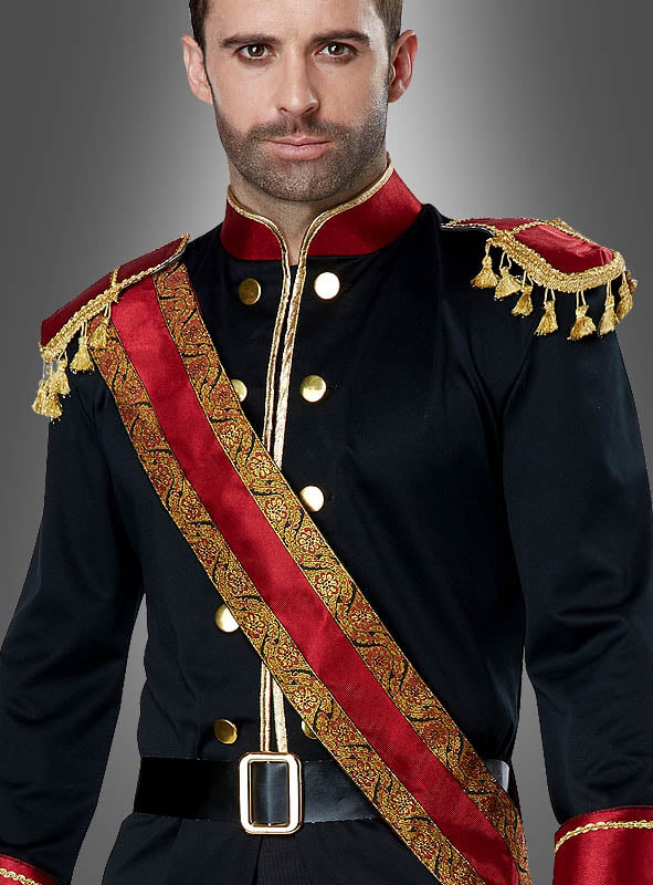 Ein Mann, der das „Dunkler Märchenprinz“-Kostüm trägt – ein schwarz-rotes Outfit im Militärstil mit goldenen Knöpfen, Schulterklappen und einer verzierten Schärpe –, steht vor einem grauen Hintergrund.