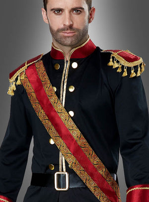 Ein Mann, der das „Dunkler Märchenprinz“-Kostüm trägt – ein schwarz-rotes Outfit im Militärstil mit goldenen Knöpfen, Schulterklappen und einer verzierten Schärpe –, steht vor einem grauen Hintergrund.