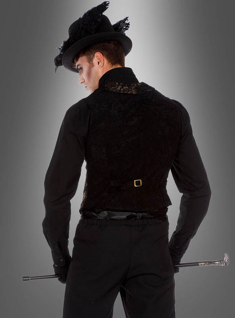 Ein Mann in schwarzer Abendgarderobe mit einem Federhut hält einen Spazierstock in der Hand und steht mit dem Rücken zur Kamera, sodass seine „Luxus Gothic Goldbrokat Weste“ vor einem grauen Farbverlauf zu sehen ist, was an klassische viktorianische Mode erinnert.