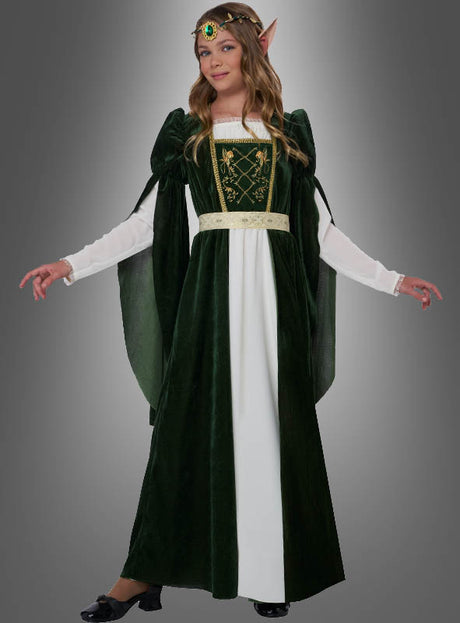 Eine Person, die das Mittelalterkleid „Elfenprinzessin Flora“ trägt – ein grün-weißes Kleid mit langen Ärmeln, einem verzierten Gürtel, spitzen Elfenohren, einem Kopfschmuck und schwarzen Schuhen –, steht vor einem grauen Hintergrund.