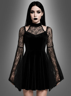Eine Frau, die das „Schwarzes Gothic Samtkleid Dakaria“ trägt – ein schwarzes Samtkleid mit Spitzen-Glockenärmeln –, steht vor einem grauen Hintergrund mit Farbverlauf und blickt mit ausdruckslosem Gesicht nach vorne.