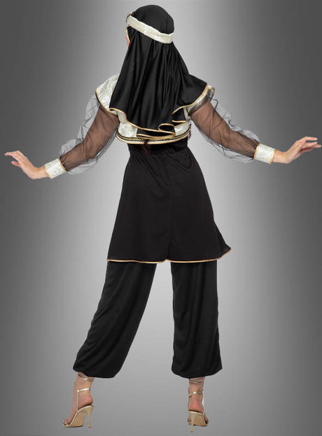 Eine Person steht mit dem Rücken zur Kamera und trägt das Kostüm „Orient Prinzessin Jasmina aus 1001 Nacht“ mit schwarzen und goldenen Details, transparenten Ärmeln, einem Kopfschmuck, einer weiten Hose und hochhackigen Schuhen vor einem grauen Hintergrund mit Farbverlauf.