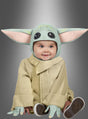 Ein Baby, das das „Baby-Yoda-Kostüm ‚Das Kind‘ Grogu aus Star Wars“ trägt – mit großen grünen Ohren und einem hellbraunen Gewand –, sitzt vor einem grauen Hintergrund mit Farbverlauf und lächelt leicht.