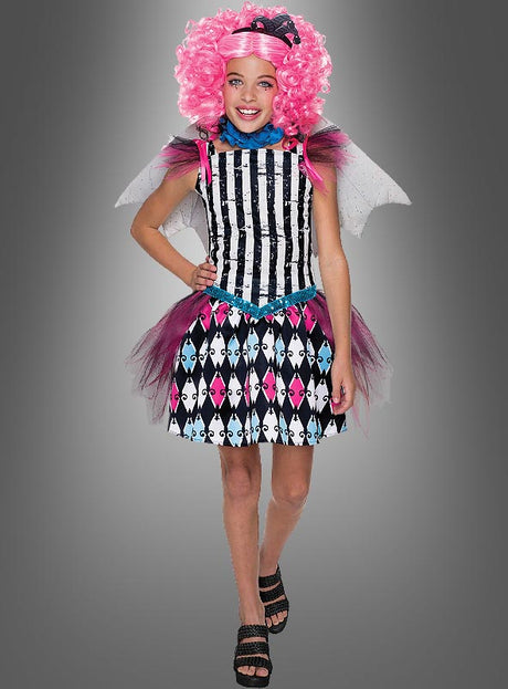 Ein Kind in einem schwarz-weiß gestreiften Kleid mit rosa Tüll, einer rosa Lockenperücke, Flügeln und einem Stirnband lächelt vor einem grauen Hintergrund und verkörpert damit perfekt den verspielten Charakter des Rochelle-Goyle-Kostüms von Monster High.
