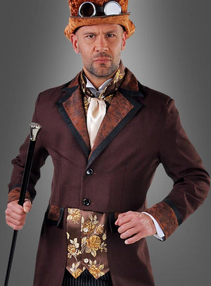 Ein Mann im „Steampunk Gentleman“-Kostüm – bestehend aus einem braunen Anzug mit Zylinder, Schutzbrille, verzierter Weste und Krawatte – steht vor einem grauen Hintergrund und hält einen schwarzen Spazierstock in der Hand. Er verkörpert damit klassische viktorianische Herrenmode, die mit unverwechselbarem Steampunk-Flair angereichert ist.