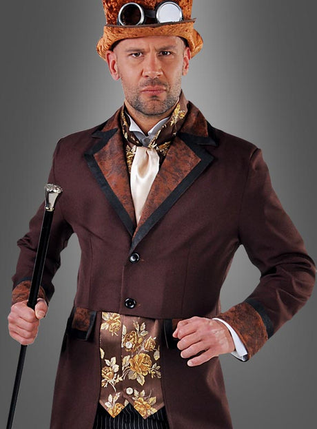 Ein Mann im „Steampunk Gentleman“-Kostüm – bestehend aus einem braunen Anzug mit Zylinder, Schutzbrille, verzierter Weste und Krawatte – steht vor einem grauen Hintergrund und hält einen schwarzen Spazierstock in der Hand. Er verkörpert damit klassische viktorianische Herrenmode, die mit unverwechselbarem Steampunk-Flair angereichert ist.