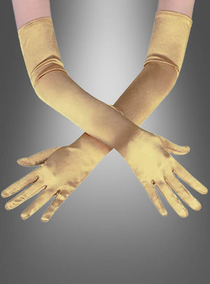 Zwei Arme, die lange, glänzende goldene Satinhandschuhe in verschiedenen Farben tragen, sind an den Handgelenken vor einem grauen Hintergrund mit Farbverlauf gekreuzt.