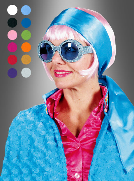Eine Person mit einem blauen Haarband-Halstuch aus Satin, das als Retro-Kopftuch gestylt ist, einer blauen Glitzer-Sonnenbrille, einer rosa Perücke und einem rosa Hemd, dazu eine strukturierte blaue Jacke aus schimmerndem Satinstoff; links sind Farbmuster zu sehen – ein lebhafter Look, perfekt für jede 70er-Jahre-Party.