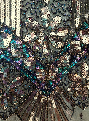 Nahaufnahme eines Stoffes, der mit schillernden Paillettenmustern in floralen und geometrischen Motiven auf einem Netzhintergrund bestickt ist und an die „Luxus 1920er Jahre Kleider Shirley“ erinnert.
