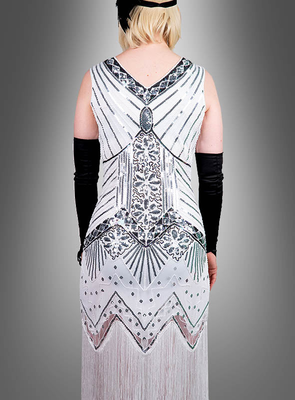Eine Person, die das „Luxus 1920er Jahre Kleider Shirley“ trägt – ein weiß-silbernes Flapper-Kleid mit Perlenstickerei und geometrischem Paillettenmuster –, kombiniert mit langen schwarzen Handschuhen und einem schwarzen Stirnband, von hinten gesehen. Diese elegante Hommage an die Mode der 1920er Jahre ist auch in Übergrößen erhältlich.