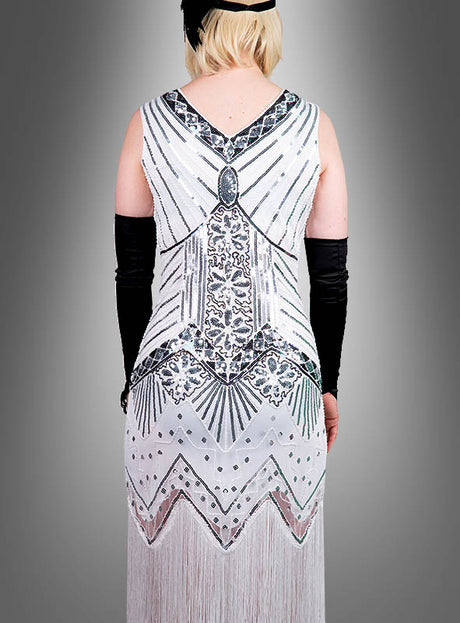 Eine Person, die das „Luxus 1920er Jahre Kleider Shirley“ trägt – ein weiß-silbernes Flapper-Kleid mit Perlenstickerei und geometrischem Paillettenmuster –, kombiniert mit langen schwarzen Handschuhen und einem schwarzen Stirnband, von hinten gesehen. Diese elegante Hommage an die Mode der 1920er Jahre ist auch in Übergrößen erhältlich.