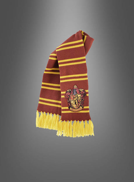 Ein rotbraun-gelb gestreifter Schal mit einem Wappen-Aufnäher und gelben Fransen wird vor einem grauen Hintergrund mit Farbverlauf präsentiert – dieser „Harry Potter Deluxe Gryffindor Schal mit Wappen“ ist das ideale Kostümzubehör für jeden Fan, der seinen magischen Look vervollständigen möchte.