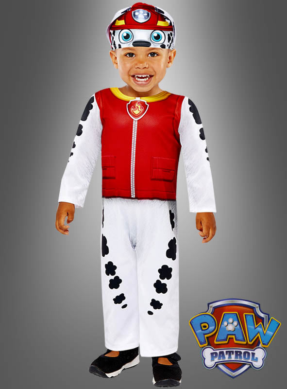 Ein Kind trägt das „Paw Patrol“-Marshall-Kostüm „Dalmatiner-Hund“, bestehend aus einer roten Weste, einer weißen Hose mit schwarzen Flecken, die an ein Dalmatiner-Kostüm angelehnt sind, sowie einer passenden Mütze. Das „Paw Patrol“-Logo ist in der rechten unteren Ecke zu sehen.