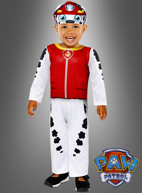 Ein Kind trägt das „Paw Patrol“-Marshall-Kostüm „Dalmatiner-Hund“, bestehend aus einer roten Weste, einer weißen Hose mit schwarzen Flecken, die an ein Dalmatiner-Kostüm angelehnt sind, sowie einer passenden Mütze. Das „Paw Patrol“-Logo ist in der rechten unteren Ecke zu sehen.