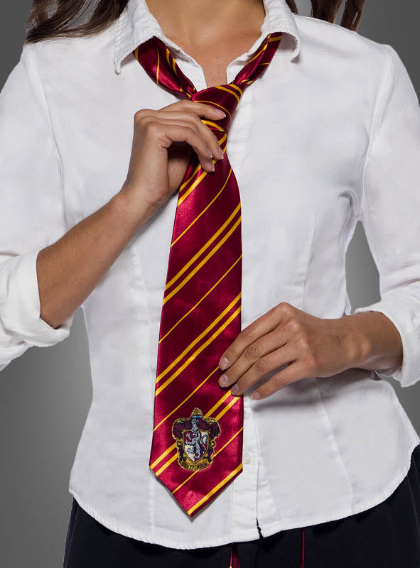 Eine Person in einem weißen Hemd richtet die Gryffindor-Krawatte mit Wappen – mit roten und goldenen Streifen und einem Wappen an der Spitze – vor einem grauen Hintergrund zurecht – ideal, um Ihre Hogwarts-Schuluniform oder Ihr Harry-Potter-Kostüm zu vervollständigen.