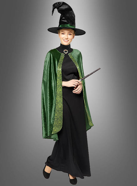 Eine Person, die das Professor-McGonagall-Kostüm für Damen trägt – bestehend aus einem langen schwarzen Kleid, einem grünen Samtumhang und einem spitzen Hexenhut – steht mit einem Zauberstab in der Hand vor einem grauen Hintergrund mit Farbverlauf.
