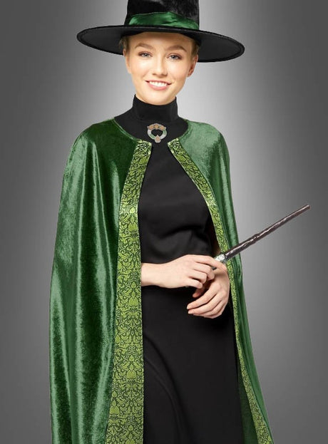 Eine Person, die das Professor-McGonagall-Kostüm für Damen trägt – bestehend aus einem grünen Samtumhang und einem breitkrempigen Hut –, hält einen Zauberstab in der Hand und lächelt vor einem grauen Hintergrund.