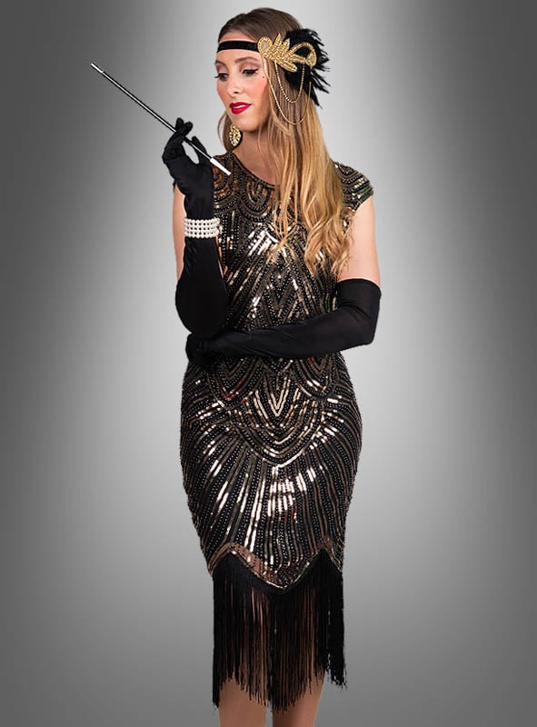Eine Frau, die das „Funkelndes Gatsby Kleid Daisy“ trägt – ein funkelndes schwarz-goldenes Flapper-Kleid im Stil der 1920er Jahre –, kombiniert mit schwarzen Handschuhen und einem mit Federn verzierten Stirnband, hält eine lange Zigarettenspitze in der Hand und steht vor einem grauen Hintergrund mit Farbverlauf.