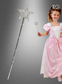 Ein junges Mädchen in einem rosa Prinzessinnenkleid und mit einer Tiara hält den schimmernden Zauberstab „Estelle Stern“ in der Hand – ein bezauberndes Accessoire, das sich perfekt als Kostümzubehör für jedes Märchenabenteuer eignet. Links ist eine Nahaufnahme des Zauberstabs vor einem grauen Hintergrund mit Farbverlauf zu sehen.
