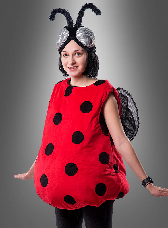 Eine Person, die ein leuchtend rotes, rundes Plüsch-Marienkäfer-Kostüm trägt, das mit schwarzen Punkten, Netzflügeln und einem Stirnband mit Fühlern und großen silbernen Augen verziert ist, steht vor einem grauen Hintergrund mit Farbverlauf – damit ist es das ideale, bezaubernde Glücksbringer-Kostüm für jeden Straßenkarneval.