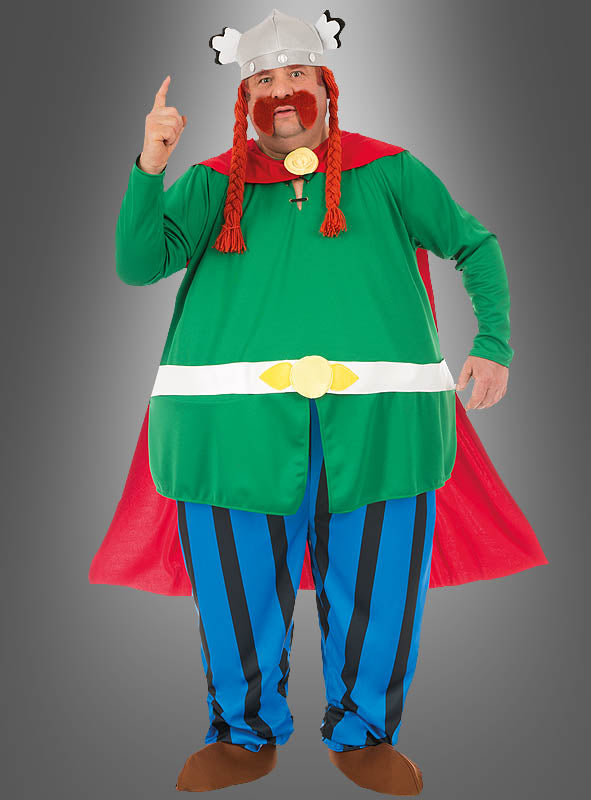 Eine Person, die das Deluxe-Majestix-Originalkostüm aus „Asterix“ trägt – bestehend aus einer grünen Tunika, einem roten Umhang, blau-weiß gestreiften Hosen, roten Zöpfen und einem geflügelten Helm –, steht vor einem grauen Hintergrund und zeigt nach oben.