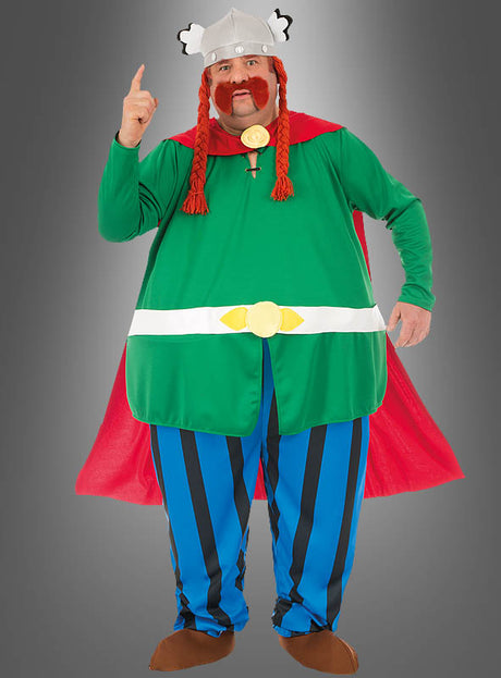 Eine Person, die das Deluxe-Majestix-Originalkostüm aus „Asterix“ trägt – bestehend aus einer grünen Tunika, einem roten Umhang, blau-weiß gestreiften Hosen, roten Zöpfen und einem geflügelten Helm –, steht vor einem grauen Hintergrund und zeigt nach oben.
