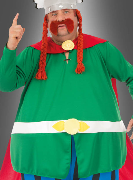 Eine Person in einem grünen Kostüm mit rotem Umhang, roter Zopfperücke, großem orangefarbenem Schnurrbart und einem silbernen Helm – ideal für alle, die das Deluxe-Majestix-Originalkostüm aus „Asterix“ suchen – zeigt mit einem Finger nach oben.