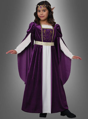 Ein junges Mädchen steht mit leicht ausgestreckten Armen vor einem grauen Hintergrund. Es trägt das „Elfenkönigin Violetta Kleid lila“ – ein lila-weißes Kleid im mittelalterlichen Stil, verziert mit einem goldenen Gürtel, einem Kopfschmuck und Elfenohren – und strahlt die magische Aura einer Elfenkönigin aus.