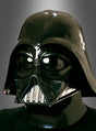 Eine Person, die den originalen Darth-Vader-Helm aus „Star Wars“ trägt – dessen glänzende Oberfläche an die Kultfigur erinnert –, steht vor einem neutralen Hintergrund mit Farbverlauf.
