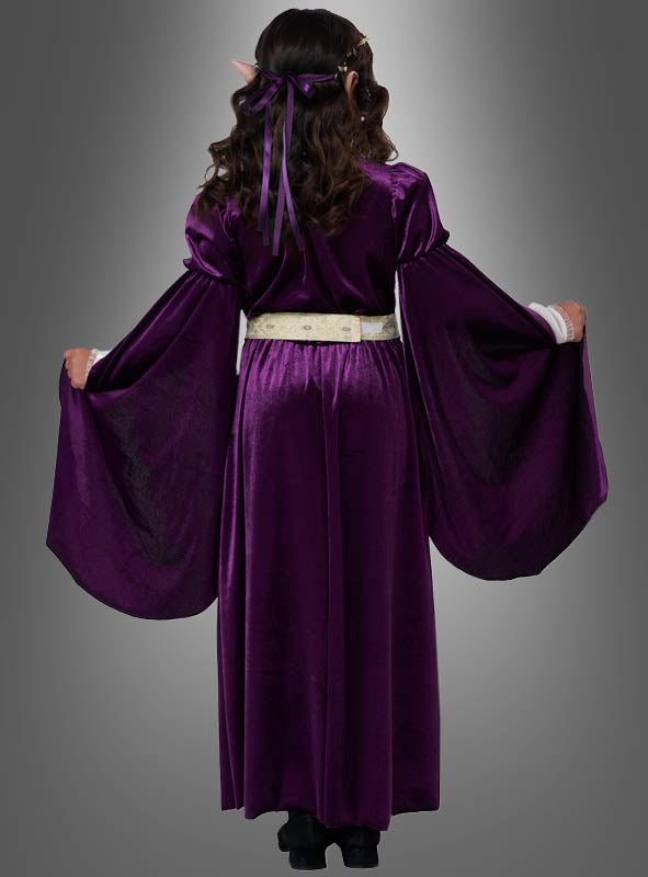 Mit dem „Elfenkönigin Violetta“-Kleid in Lila – einem langen, violetten Samtgewand mit weiten Ärmeln, einem cremefarbenen Gürtel und spitzen Ohren – ist dieser bezaubernde Look perfekt für alle, die ein märchenhaftes Kinderkostüm suchen oder ein Elfenkönigin-Kinderkostüm zum Leben erwecken möchten. Von hinten vor einem grauen Hintergrund fotografiert.