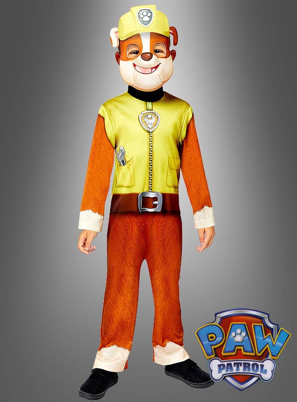 Ein Kind steht aufrecht da, die Arme an den Seiten, und trägt das Rubble-Kostüm von Paw Patrol. Das offizielle Nickelodeon-PAW-Patrol-Logo ist in der rechten unteren Ecke vor einem grauen Hintergrund mit Farbverlauf zu sehen.