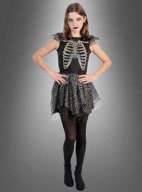 Vor einem grauen Hintergrund steht eine Person, die das „Schillerndes Skelett Kleid Mädchen“ mit seinem auffälligen Skelett-Print trägt, kombiniert mit schwarzen Strumpfhosen und dunklem Make-up – die perfekte Inspiration für alle, die auf der Suche nach einem auffälligen Halloween-Kostüm für Mädchen sind.