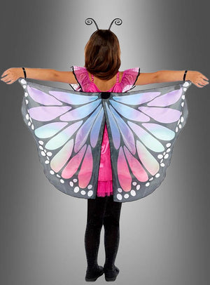 Ein Kind steht mit ausgestreckten Armen vor einem grauen Hintergrund und trägt schwarze Leggings, ein rosa Schmetterlingskleid und farbenfrohe Schmetterlingsflügel mit blauen, violetten und weißen Mustern – ein bezauberndes Schmetterlings-Traumkostüm für Kinder, das sich perfekt für fantasievolles Spielen eignet.