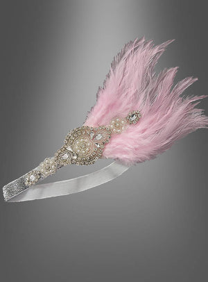 Ein „Haarband im Stil der 20er Jahre mit Strass und Perlen – Lilli“, verziert mit pinkfarbenen Federn und einem kunstvollen, funkelnden Mittelstück, wird vor grauem Hintergrund präsentiert und erinnert an den glamourösen Stil klassischer Flapper-Kleider sowie an elegante Kopfschmuck-Designs der 20er Jahre.