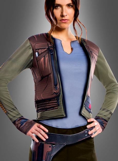 Eine Frau steht mit den Händen in den Hüften da. Sie trägt ein blaues Shirt und die „Star Wars: Rogue One – Jyn Erso“-Jacke für Erwachsene mit einem aufgedruckten Motiv auf einfarbigem grauen Hintergrund.