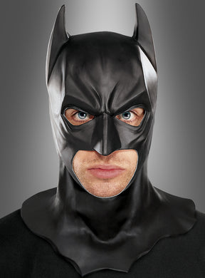 Eine Person, die die Batman-Vollmaske für Erwachsene trägt und vor einem schlichten, grau verlaufenden Hintergrund geradeaus blickt, was an den ikonischen Stil aus „The Dark Knight Rises“ erinnert.