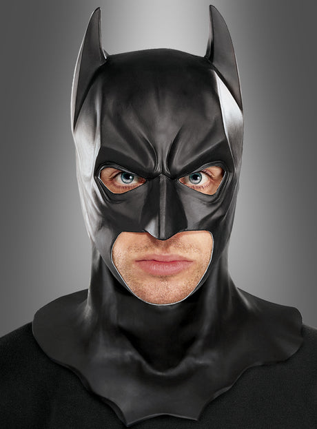 Eine Person, die die Batman-Vollmaske für Erwachsene trägt und vor einem schlichten, grau verlaufenden Hintergrund geradeaus blickt, was an den ikonischen Stil aus „The Dark Knight Rises“ erinnert.
