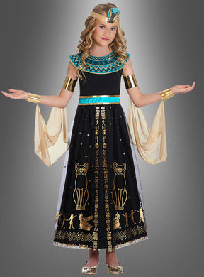 Ein junges Mädchen trägt das „Pharaonin“-Kostüm für Mädchen, bestehend aus einem ägyptisch inspirierten Kleid mit goldenen und türkisfarbenen Akzenten, einem majestätischen Kopfschmuck und Hieroglyphenmustern, und steht mit leicht ausgestreckten Armen vor einem grauen Hintergrund.