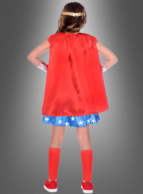 Ein als Superheldin verkleidetes Kind steht mit dem Rücken zur Kamera und trägt einen roten Umhang, einen blauen Rock mit weißen Sternen, rote Kniestrümpfe und ein goldenes Stirnband – ein kultiges klassisches Wonder-Woman-Kinderkostüm, das sich perfekt eignet, um junge Helden zu inspirieren oder jede Superheldinnen-Kostümsammlung zu vervollständigen.