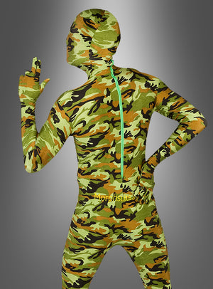 Eine Person, die einen militärischen Morphsuit-Tarnanzug trägt, der Gesicht und Hände vollständig bedeckt, steht mit einer Hand in die Hüfte gestützt und der anderen erhoben vor einem grauen Hintergrund mit Farbverlauf.