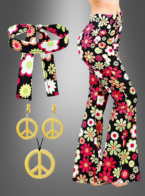 Eine Frau trägt die Schlaghose „Night Flower“ mit Accessoires, die sich durch ein fröhliches Blumenmuster und ein passendes Stirnband auszeichnet, während seitlich goldene Peace-Zeichen-Ohrringe und eine Halskette zu sehen sind.