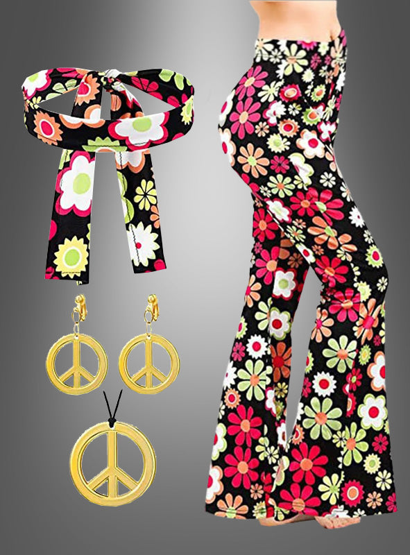 Eine Frau trägt die Schlaghose „Night Flower“ mit Accessoires, die sich durch ein fröhliches Blumenmuster und ein passendes Stirnband auszeichnet, während seitlich goldene Peace-Zeichen-Ohrringe und eine Halskette zu sehen sind.