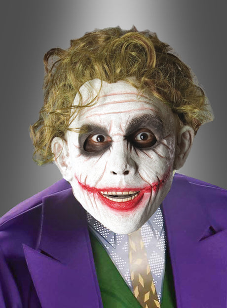 Eine Person mit weißem Gesichts-Make-up, geschwärzten Augen und roten Lippen, die zu einem breiten Grinsen verzogen sind, sowie einer violetten Jacke und einer grünen Weste ähnelt einem Comic-Bösewicht, der in einem auffälligen Joker-Kostüm, komplett mit der Original-Joker-Perücke, zum Leben erweckt wurde.