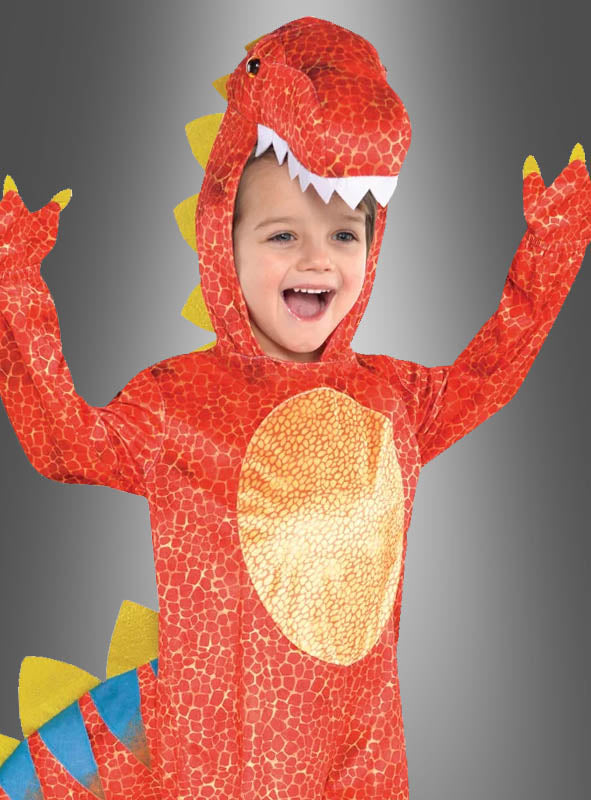 Ein Kind, das das rote Dinosaurier-Kinderkostüm „Dinomite“ trägt – mit gelben Stacheln und einer Kapuze in Form eines Dinosaurierkopfes –, steht mit erhobenen Armen und einem Lächeln da – bereit, beim Kinderkarneval zu beeindrucken.