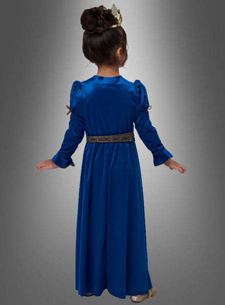 Ein junges Mädchen mit hochgesteckten Haaren und einer Krone trägt das „Kleine Renaissance-Prinzessin“-Kostüm – ein langärmeliges, blaues Samtkleid für Kinder – und steht mit dem Rücken zum Betrachter vor einem grau verlaufenden Hintergrund.
