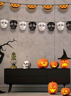 Ein modernes Zimmer, das zu Halloween mit Kürbislaternen, einem Totenkopf, einer Laterne, einem Hexenhut und den festlichen Halloween-Girlanden mit Kürbis- oder Totenkopfmotiven geschmückt ist, die an der Betonwand hängen.