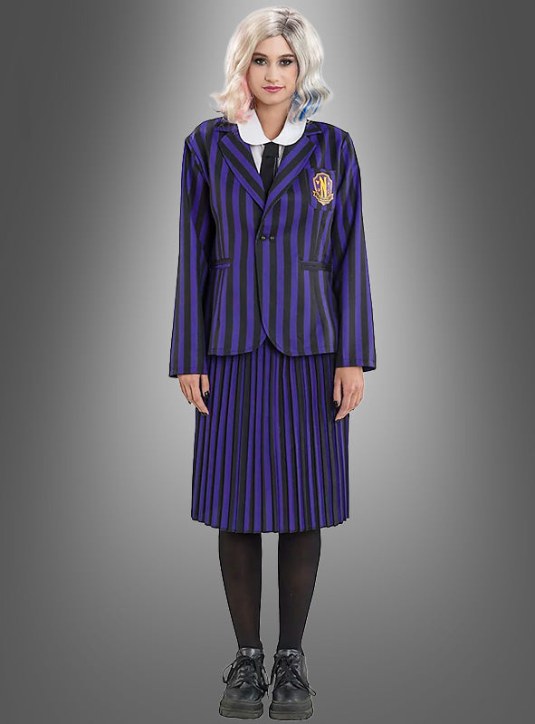 Diese Person trägt das Enid-Kostüm aus „Wednesday“ – bestehend aus einer schwarz-lila gestreiften Schuluniform mit Blazer und Rock, einem weißen Hemd, einer schwarzen Krawatte, schwarzen Strumpfhosen, schwarzen Schuhen und einer weißen Perücke – und verkörpert damit den ikonischen Look der Nevermore Academy, während sie vor einem grauen Hintergrund steht.