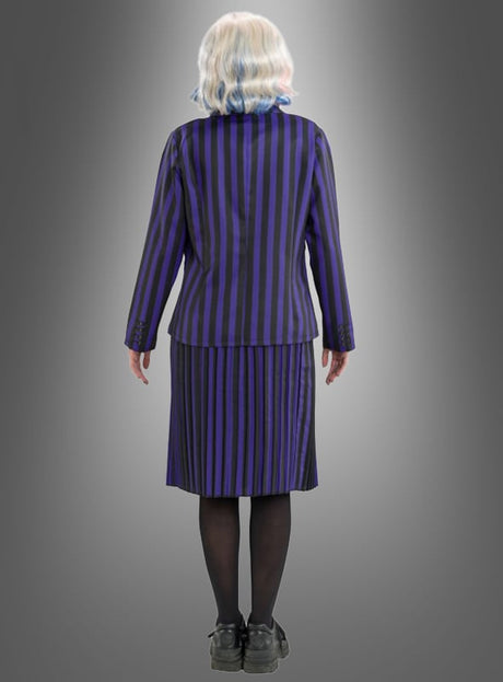 Eine Person mit kurzen, gewellten, weißen Haaren steht mit dem Rücken zur Kamera und trägt das „Enid-Kostüm aus Wednesday“ – ein schwarz-lila gestreiftes Set aus Jacke und Rock –, dazu schwarze Strumpfhosen und schwarze Schuhe, vor einem grauen Hintergrund mit Farbverlauf.