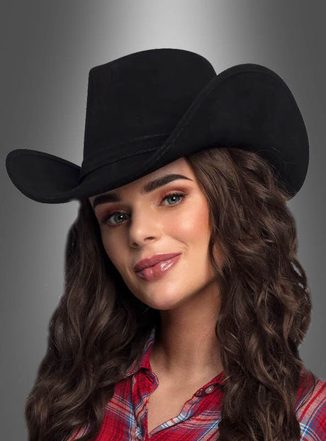 Frau mit langen braunen Haaren, die einen Cowboyhut „Wild Lederoptik Deluxe“ und ein rotes Karohemd trägt und vor einem grauen Hintergrund mit Farbverlauf posiert.