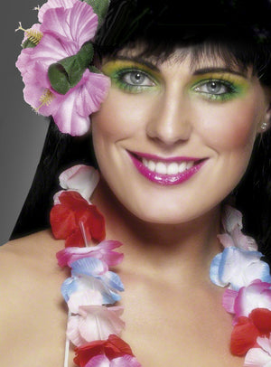 Eine Frau, die „Hawaii Blumen“-Haarschmuck – ein farbenfrohes Haaraccessoire mit Blumenmotiv – trägt, dazu eine rosa Blume im Haar, leuchtend grünen Lidschatten und rosa Lippenstift, lächelt in die Kamera und präsentiert so den perfekten Look für ein Hawaii-Kostüm oder eine Hawaii-Party.